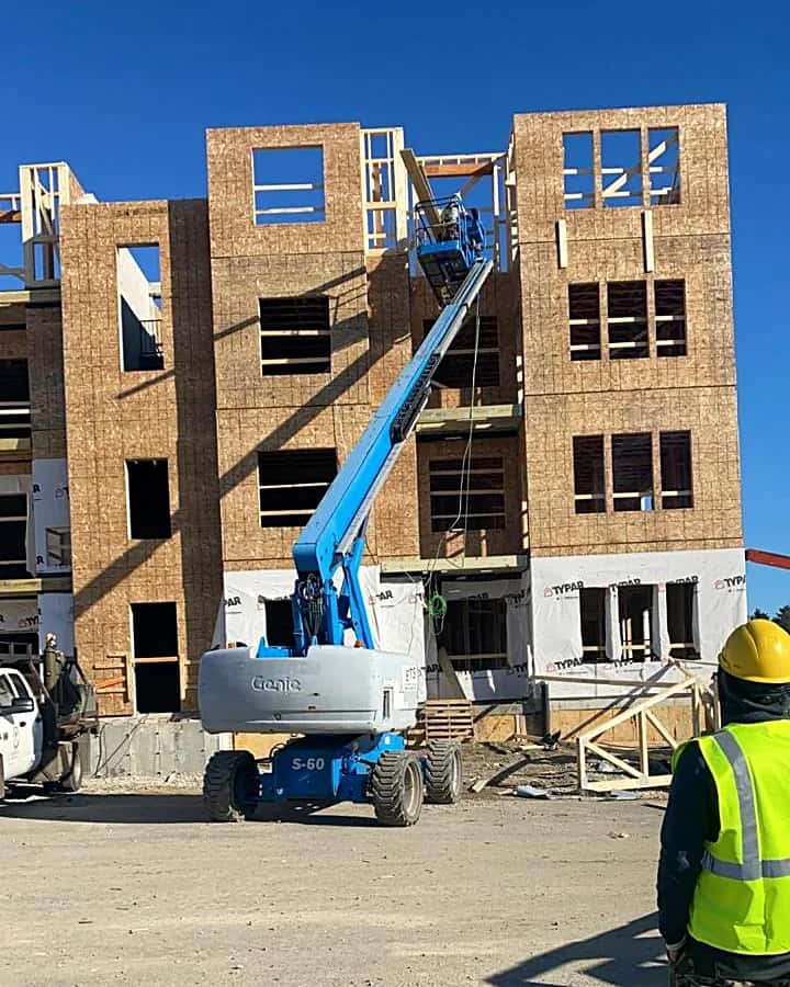 Multi-story wood-frame residential building under construction, with a boom lift on site