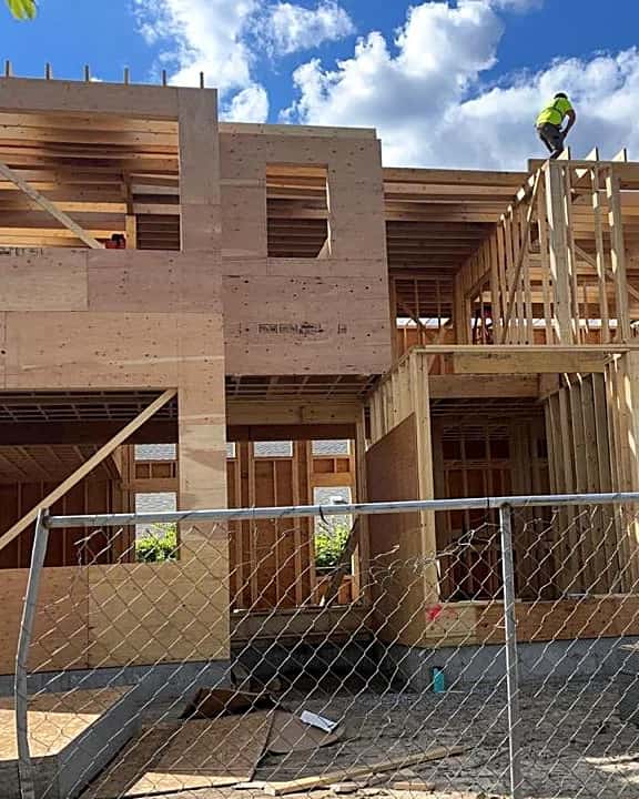 Two-story house in the framing stage behind a construction fence