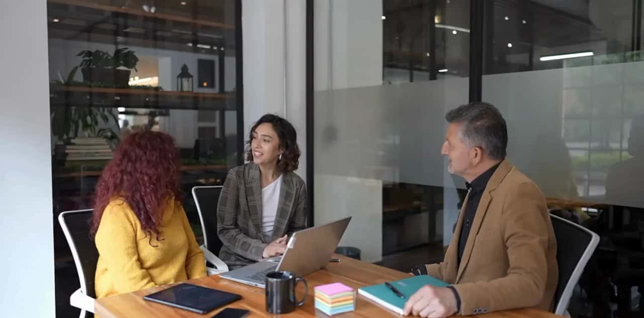 Three people discussing a project around a meeting table